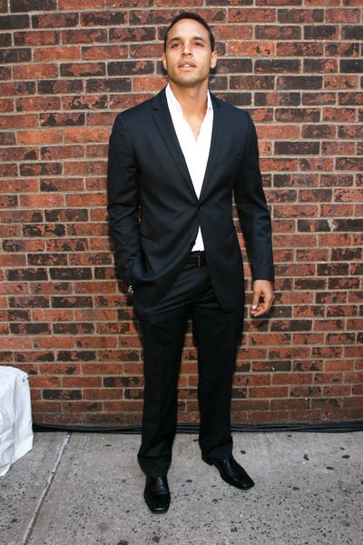 Daniel Sunjata in a white shirt and black suit.